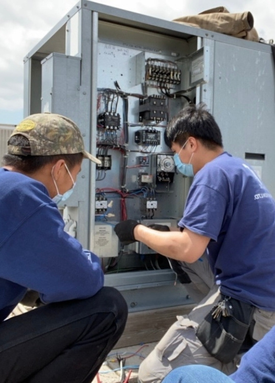 Commercial refrigeration technicians servicing an outdoor electrical control panel for cooling equipment.